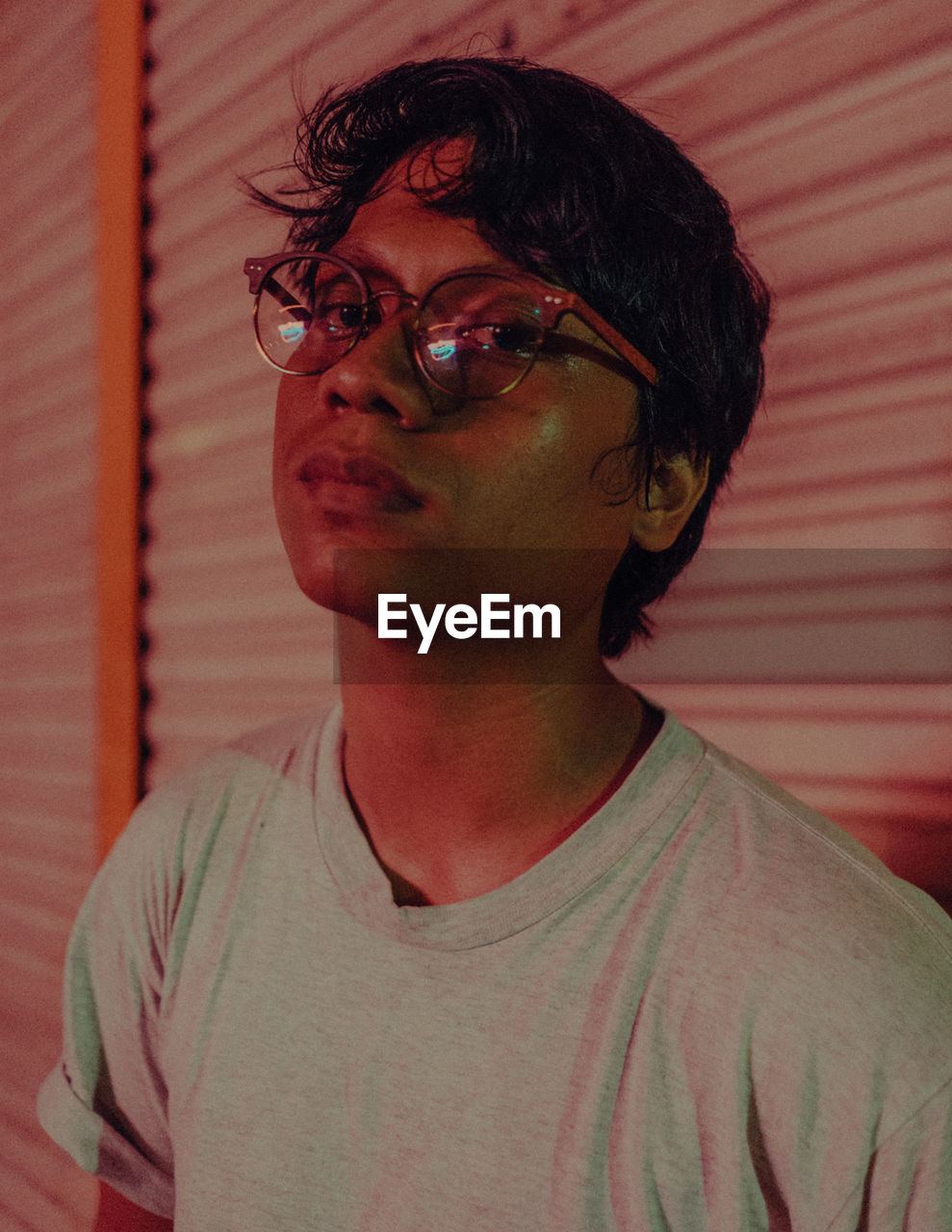 Portrait of young man wearing eyeglasses against closed shutter