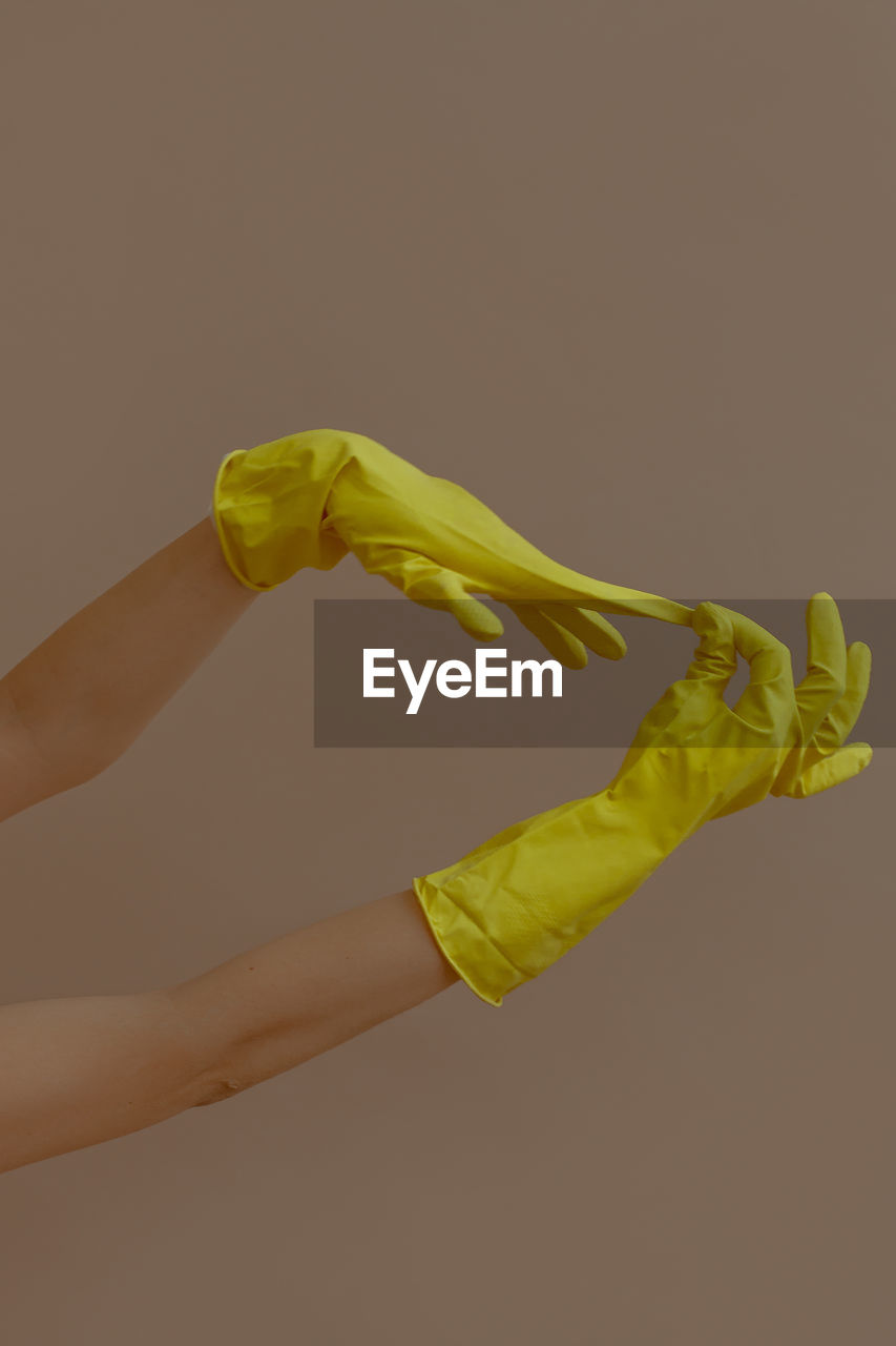 Cropped hands of person removing yellow gloves against beige background