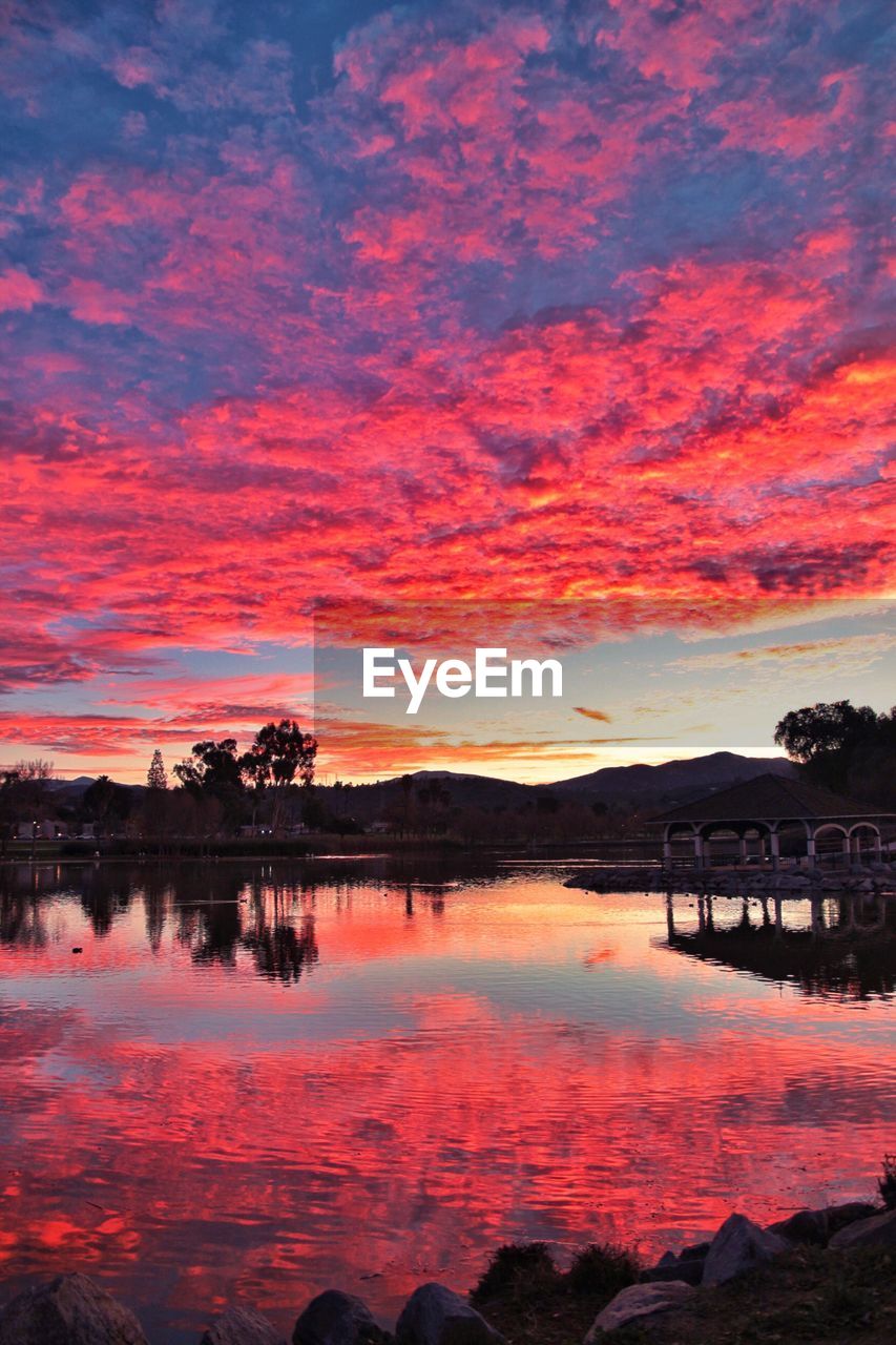 Scenic view of lake against dramatic sky during sunset