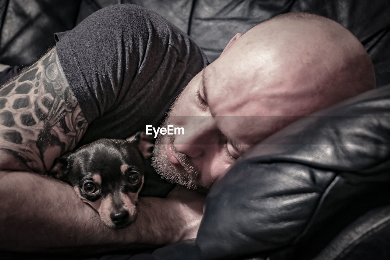 Close-up of man with dog sleeping on sofa at home
