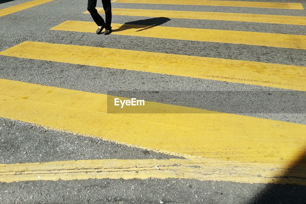 Low section of person walking on zebra crossing during sunny day