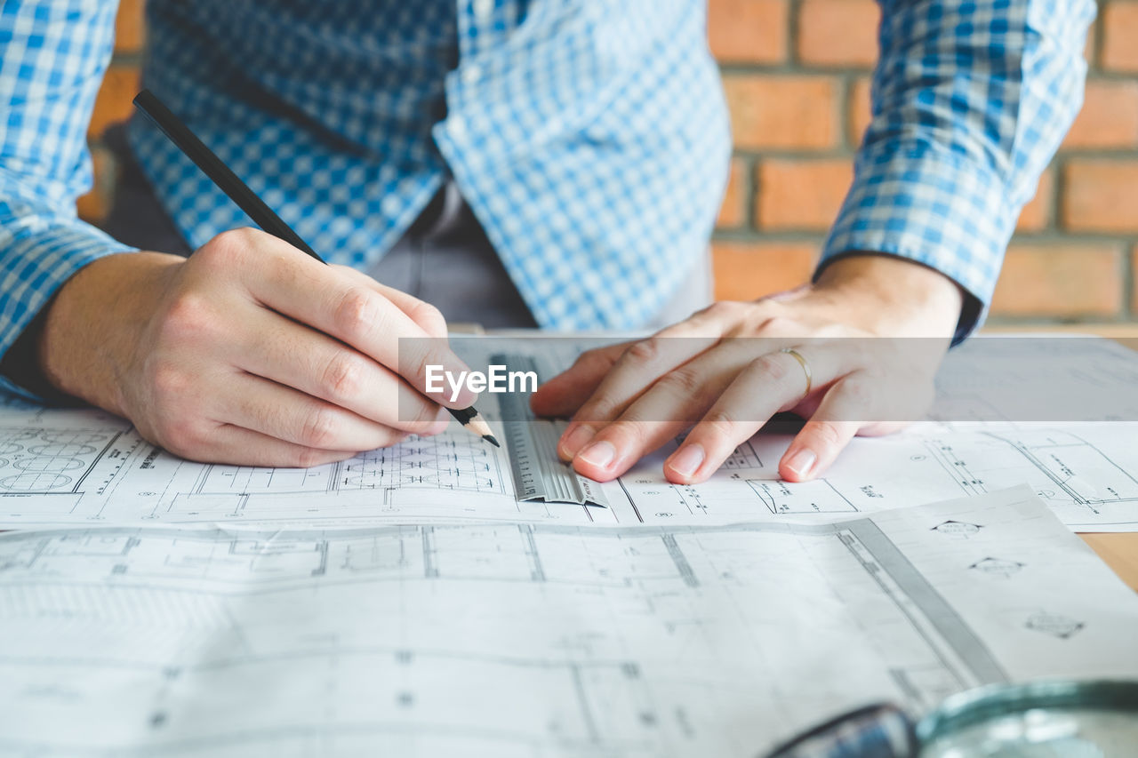 Midsection of man drawing on blueprint at desk