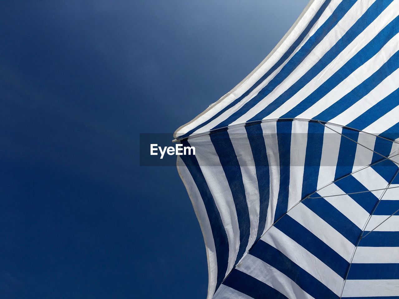 Low angle view of white and blue beach umbrella against blue sky