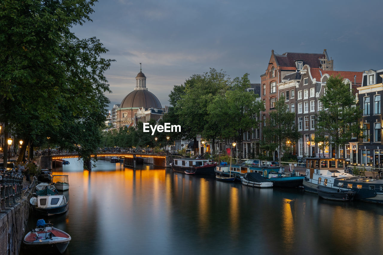Amsterdam canal at dusk with boats, canal houses, church spire in warm light, serene atmosphere