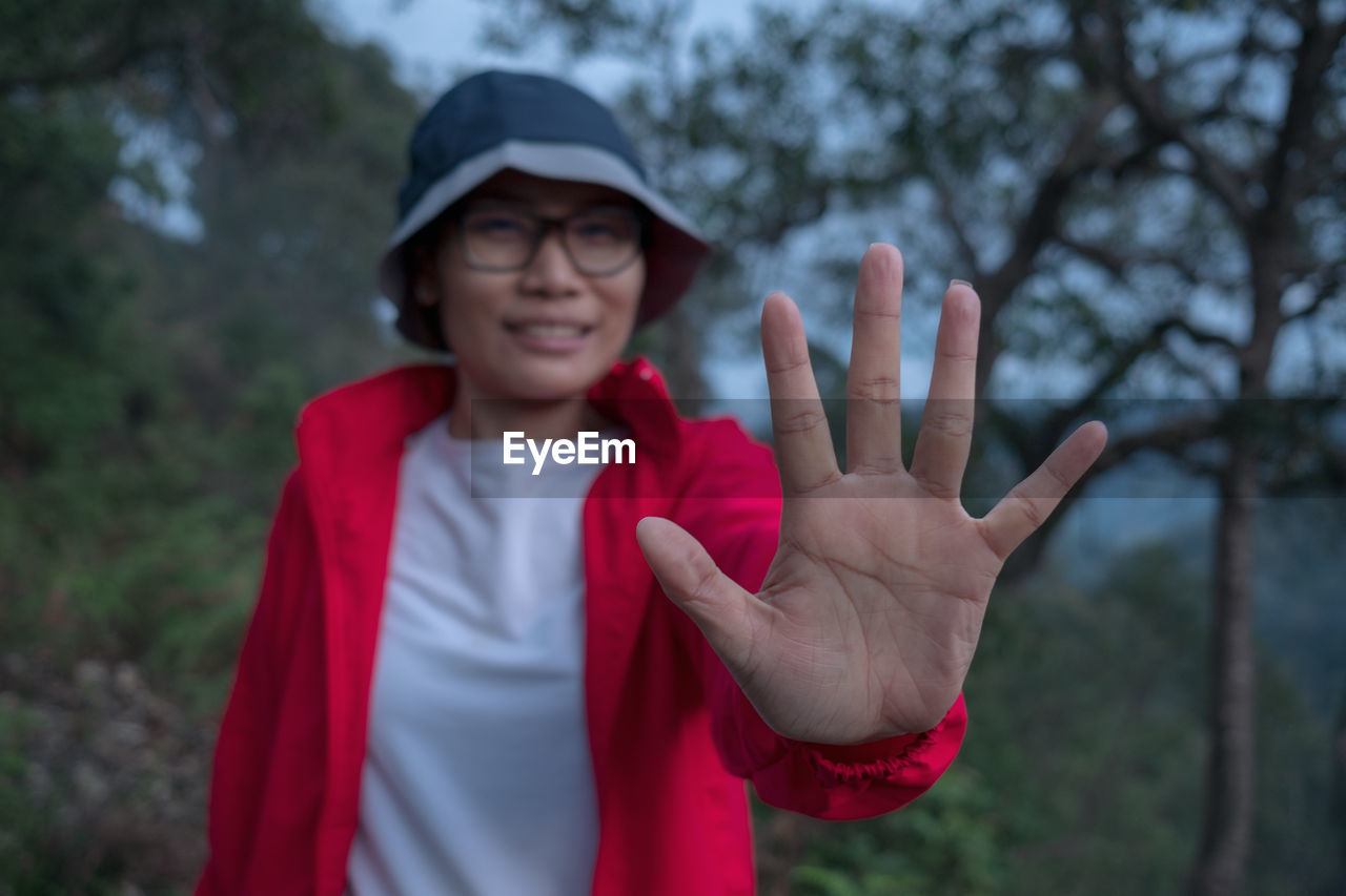 Portrait of woman gesturing stop sign against trees