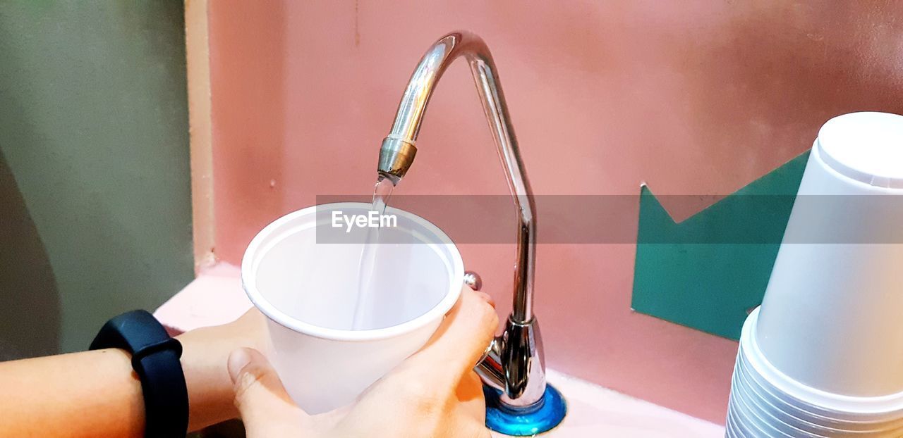 Cropped hands of person filling water in disposable cup