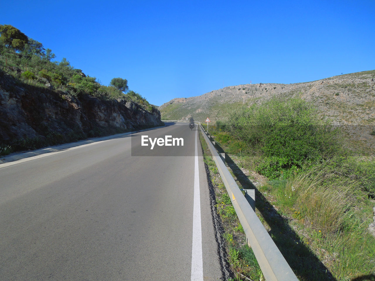 Road amidst trees against clear blue sky