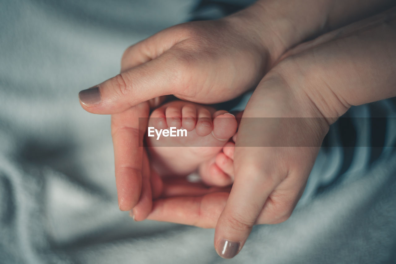 Cropped hands of woman holding baby boy feet on bed