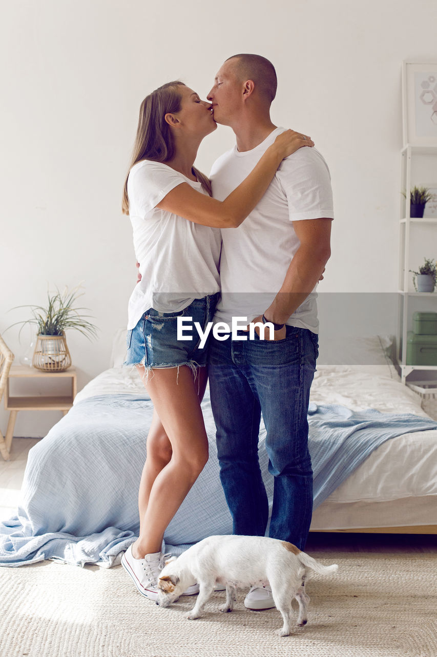 Couple in white t-shirts and blue jeans stand in a white room