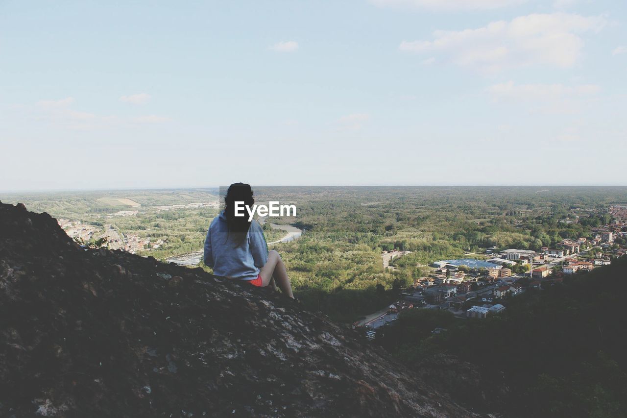 Rear view of woman sitting on landscape against sky