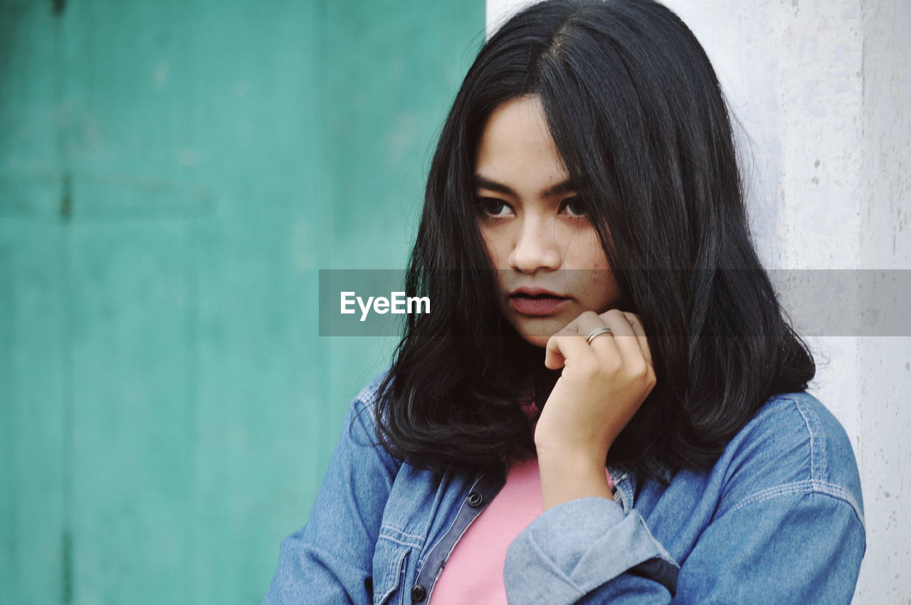 Thoughtful woman wearing denim jacket while looking away against wall