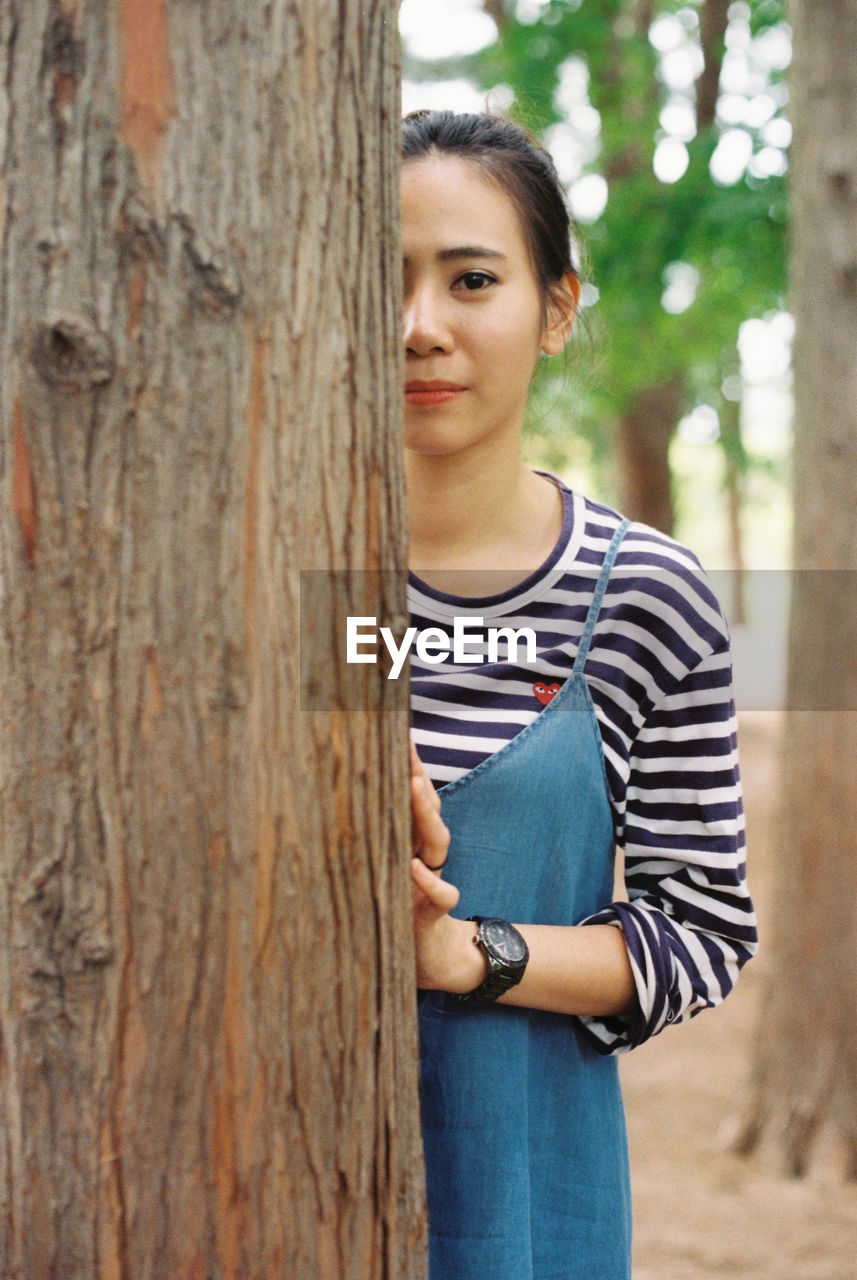 PORTRAIT OF YOUNG WOMAN STANDING ON TREE