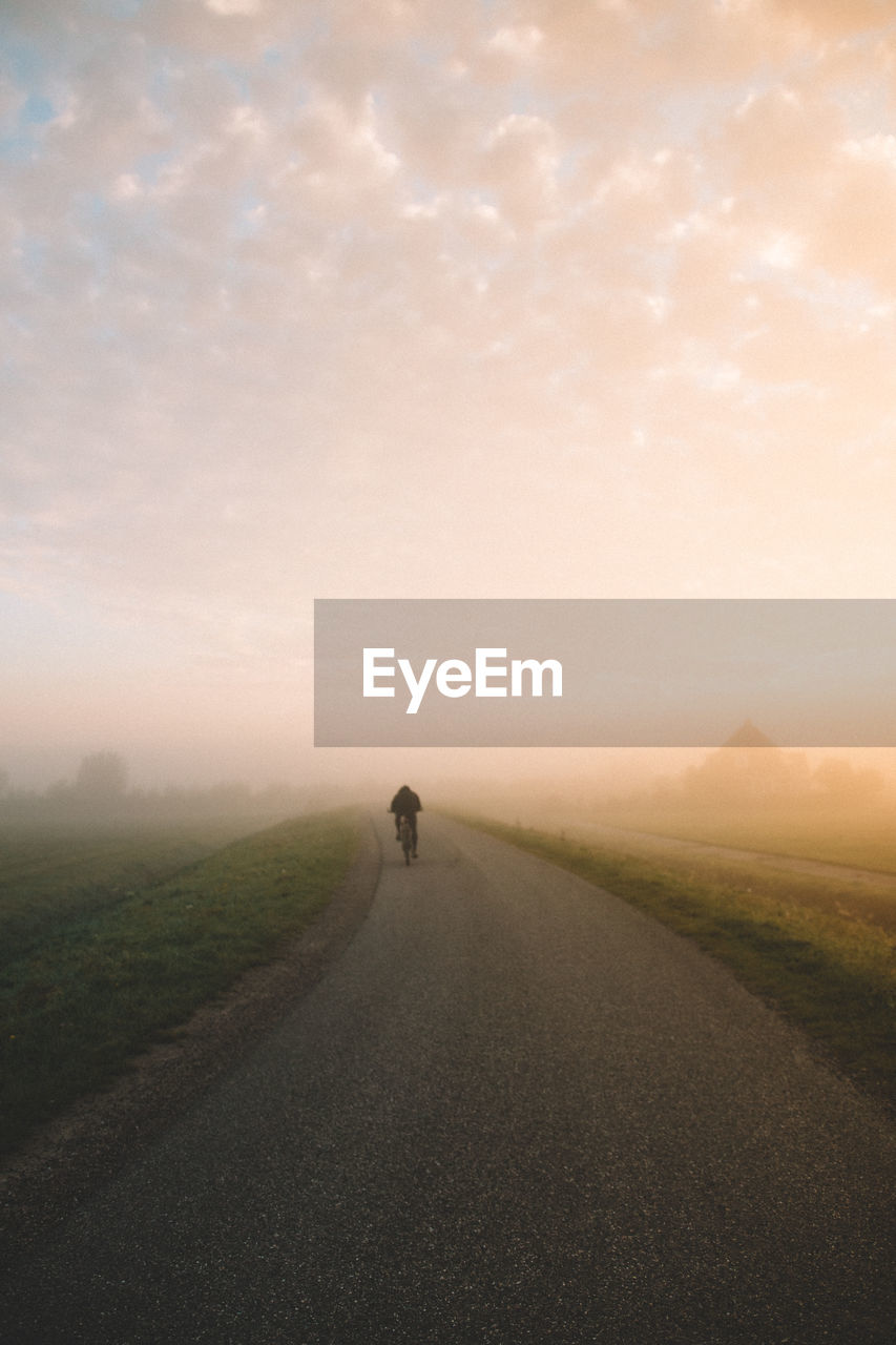 Rear view of man cycling on road during foggy weather against sky