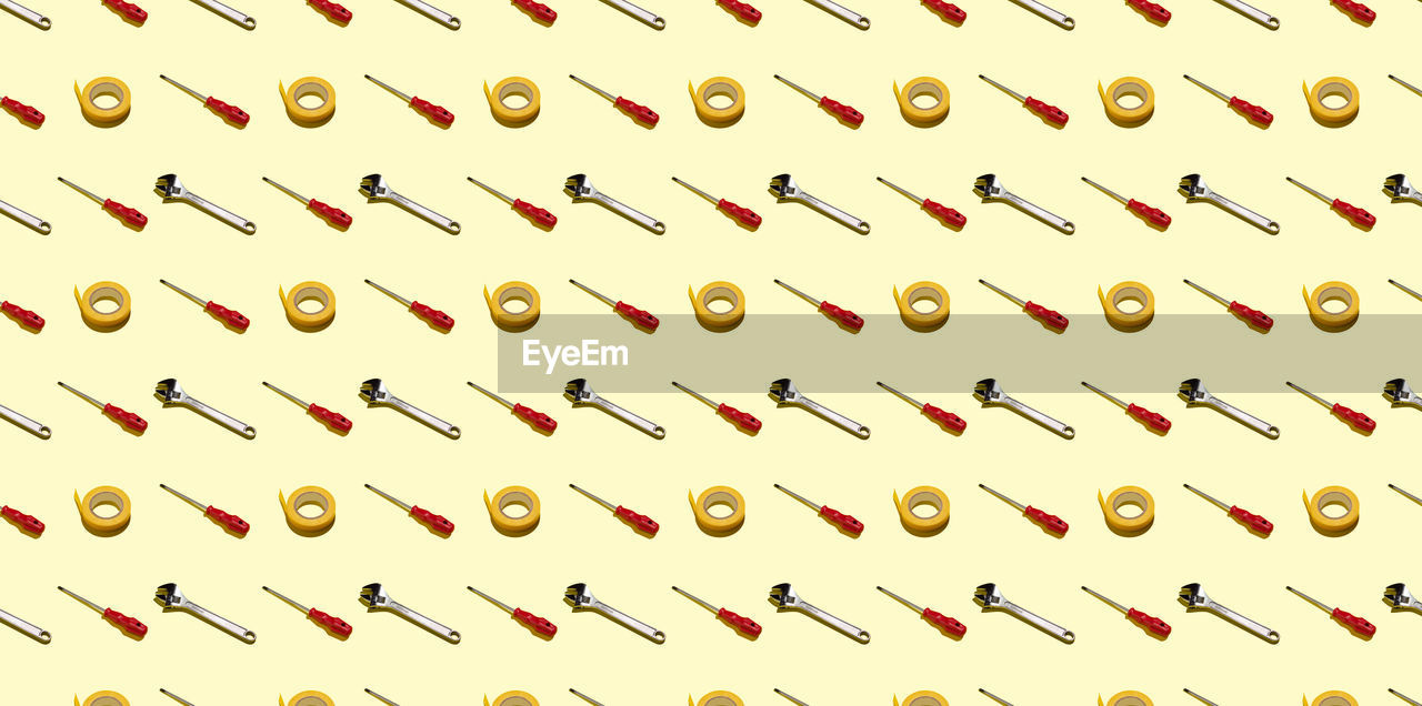 Screwdrivers, adjustable keys and electrical tape on a yellow background, pattern, hard shadows. 