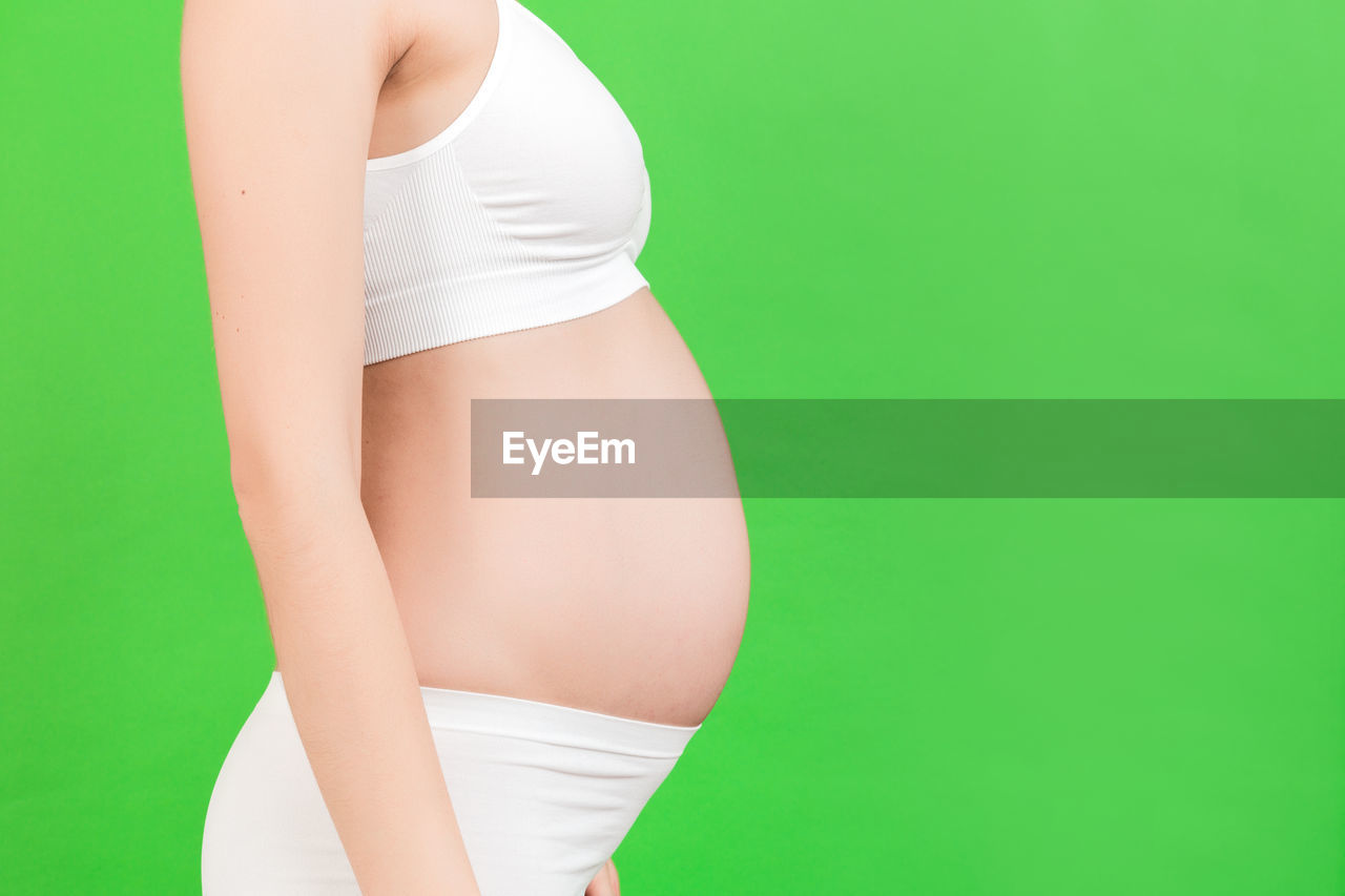 MIDSECTION OF WOMAN STANDING ON GREEN BACKGROUND