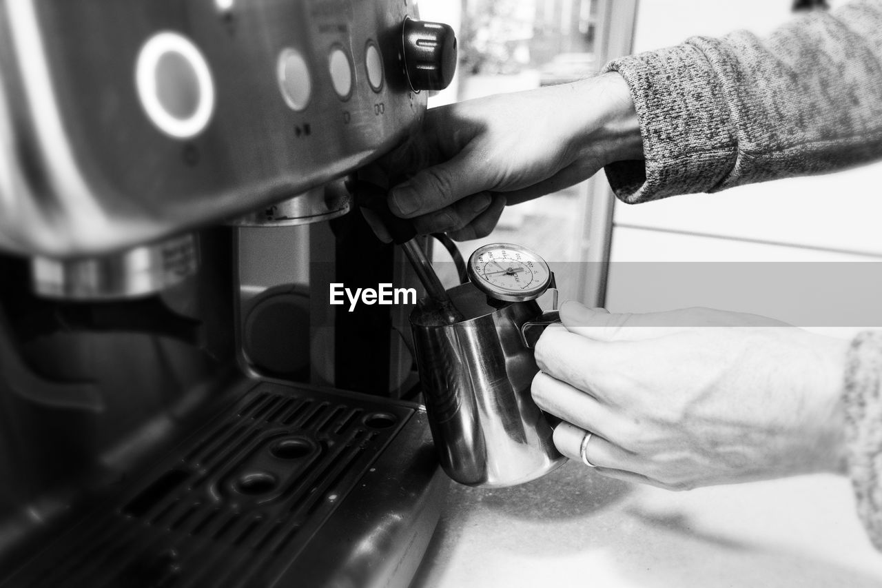 Cropped of hand preparing latte coffee, brewing machine , foaming , vintage black and white tone. 