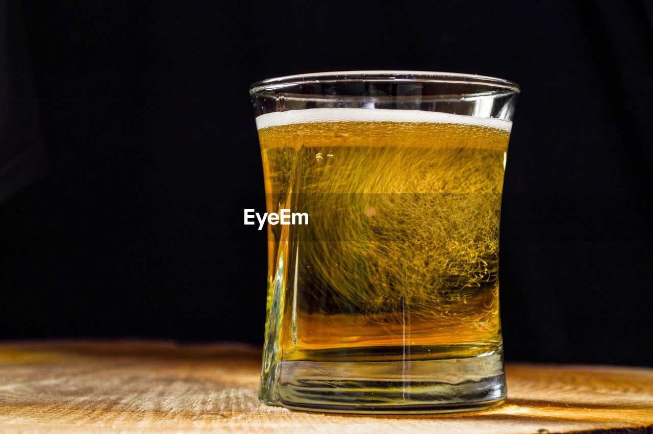 Close-up of beer in glass on table against black background