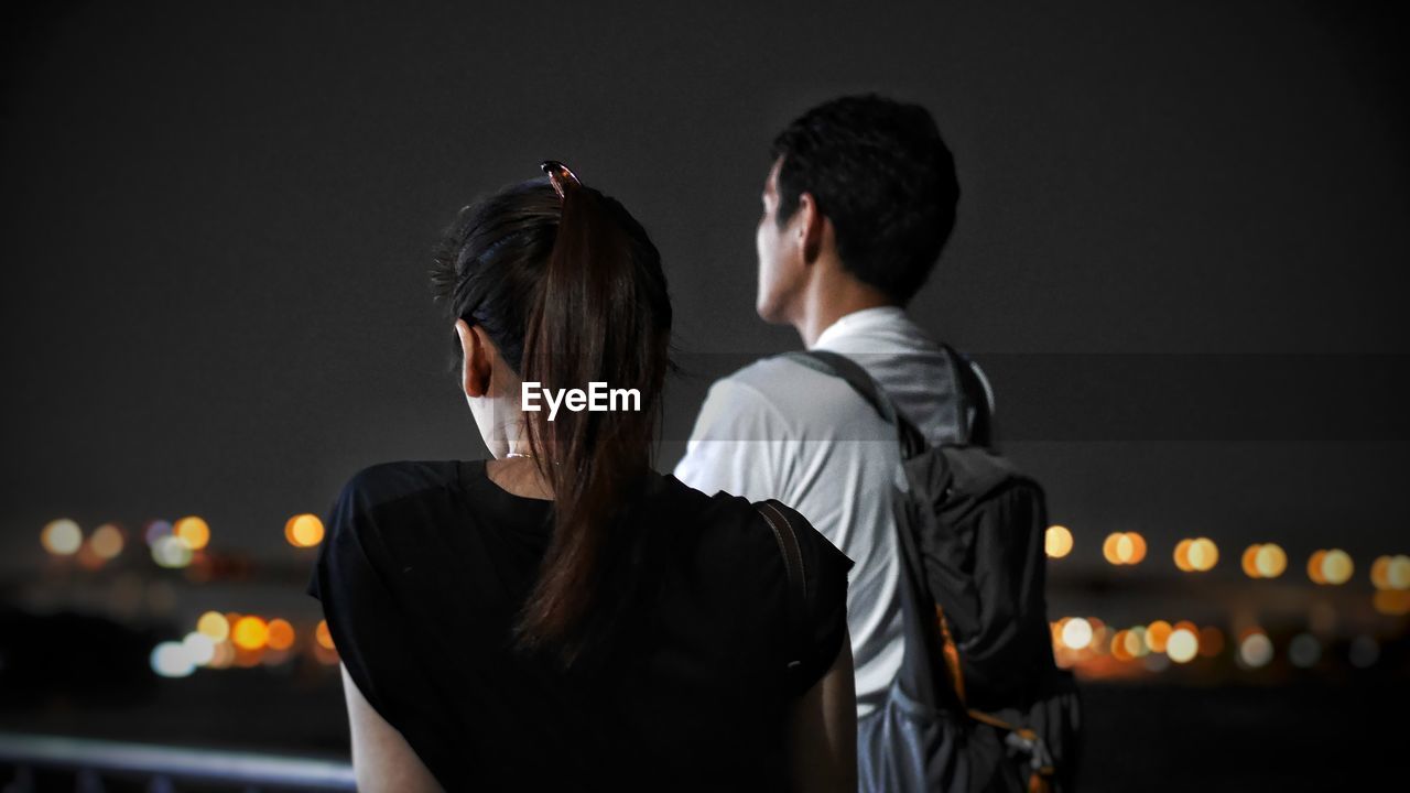 Rear view of couple standing against sky at night