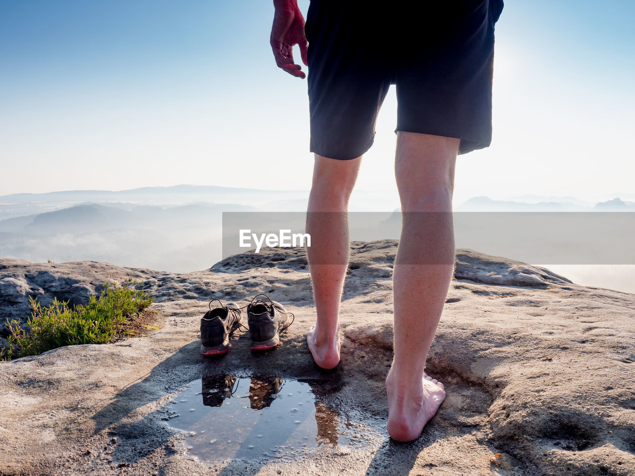 Hiker next to taken off shoes and water puddle on sandstone rock edge enjoy misty landscape view