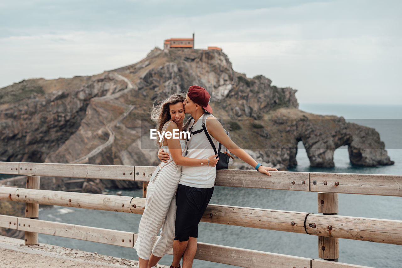 Couple embracing while standing by railing against sea