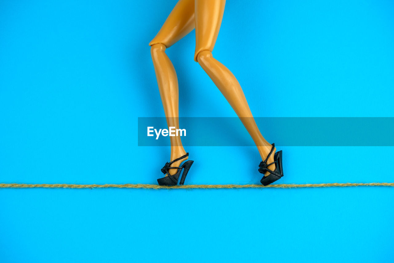 Low section of figurine walking in high heels on rope against blue background