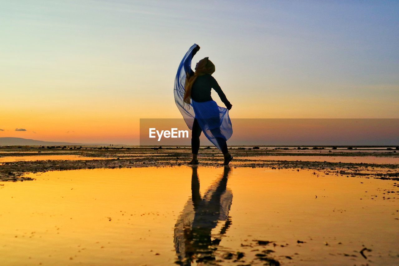 Full length of woman dancing at beach against clear sky during sunset