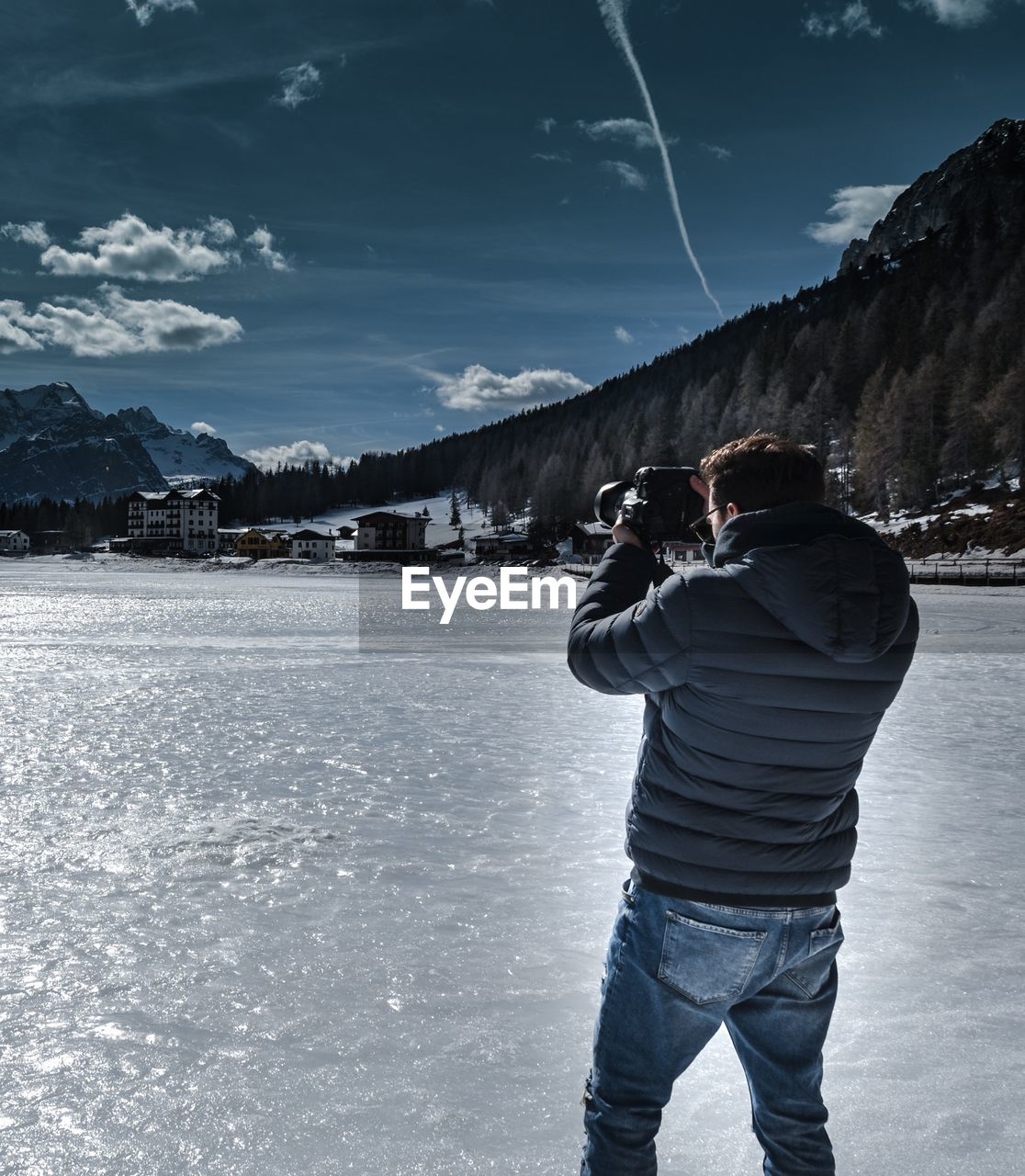 Rear view of man photographing while standing on frozen lake