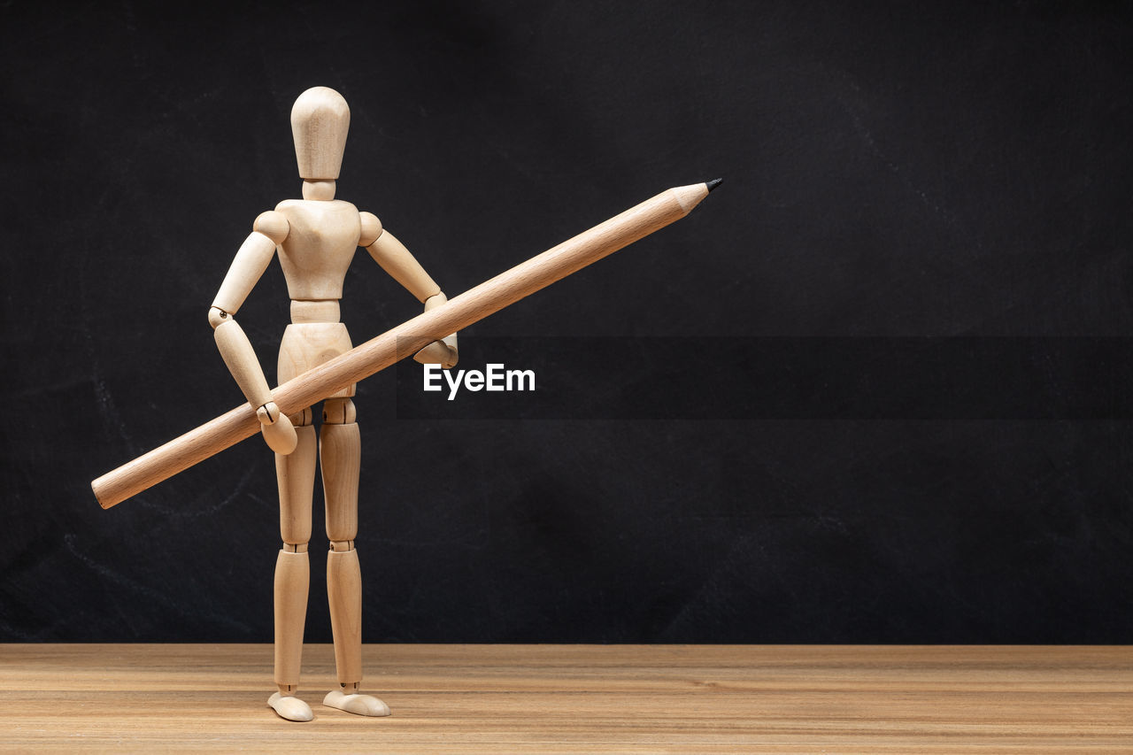 Wooden mannequin holding a pencil. blackboard background. drawing concept. copy space