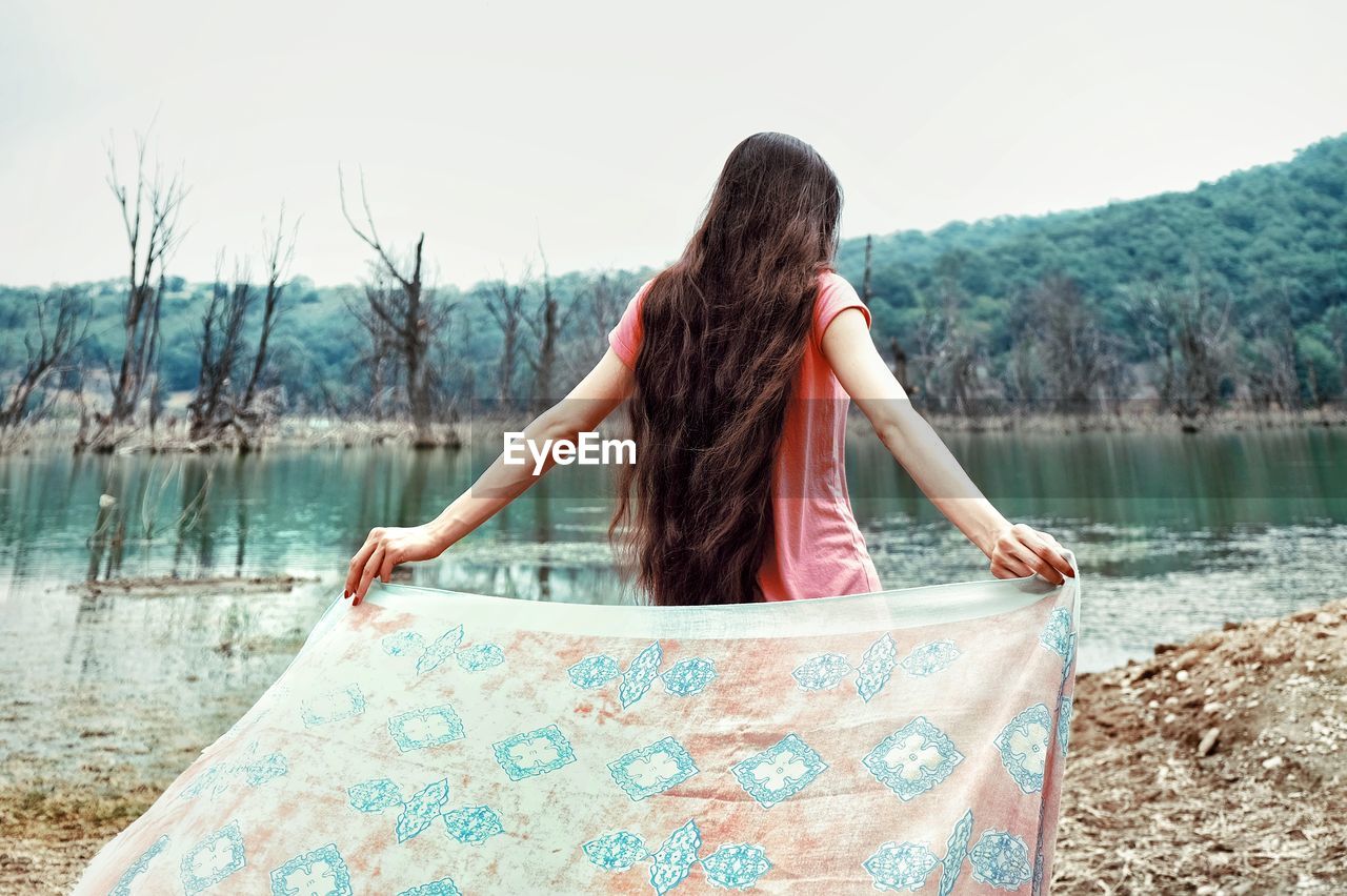 Rear view of woman with scarf standing at lakeshore