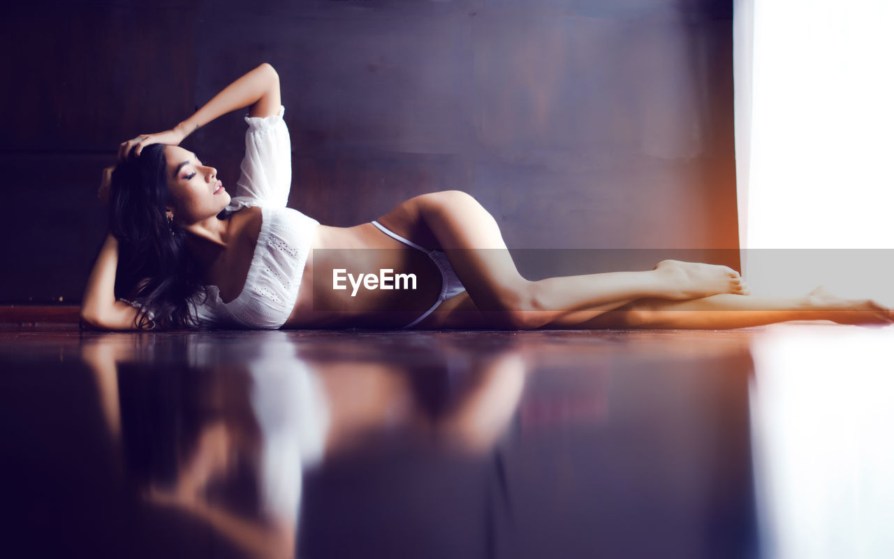 Beautiful young woman wearing bikini looking away while lying on floor