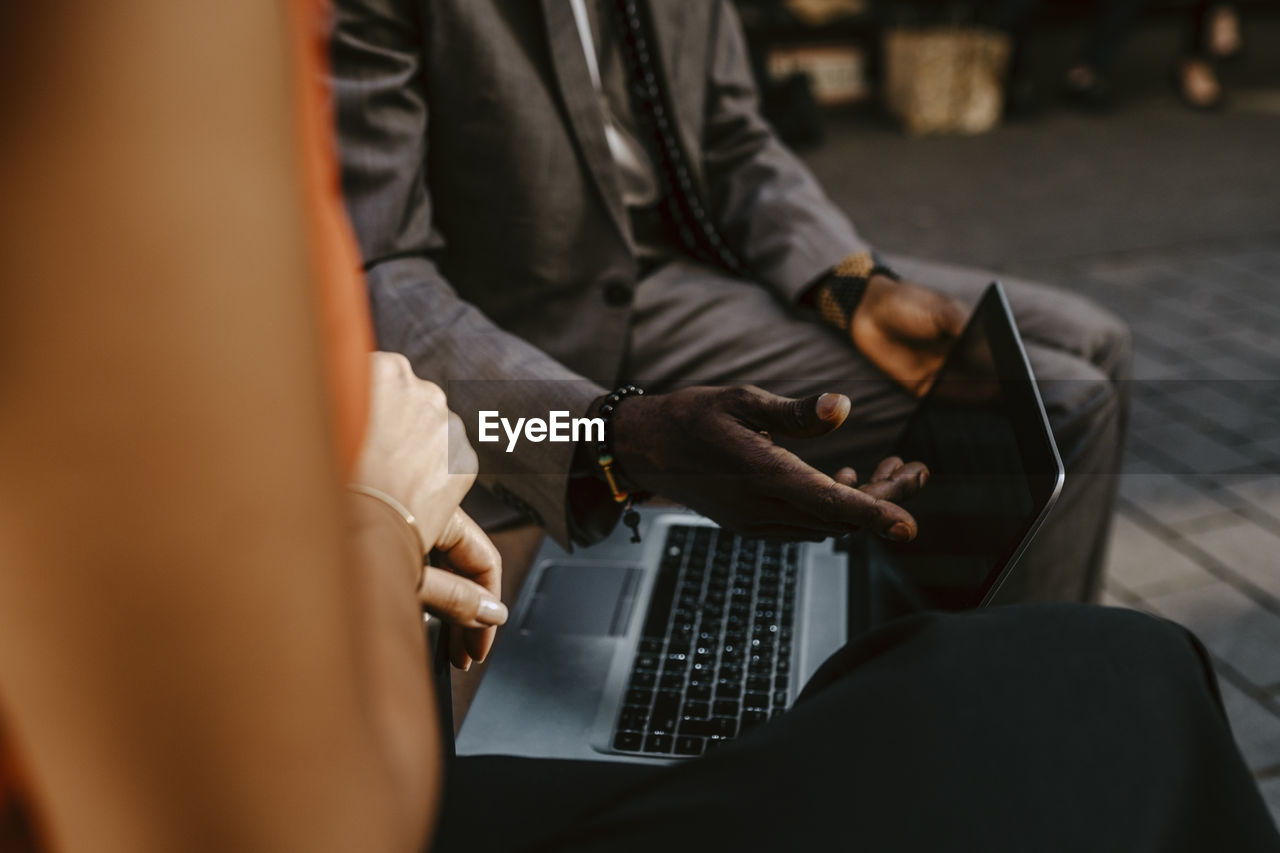 Cropped image of male entrepreneur discussing with female colleague over laptop