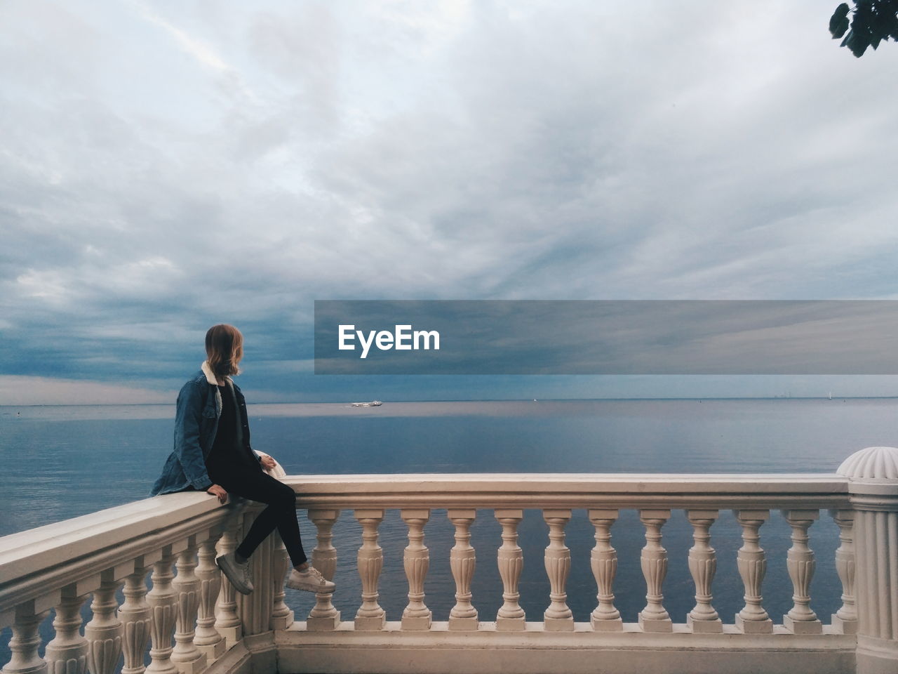 Full length of woman sitting on railing against sea