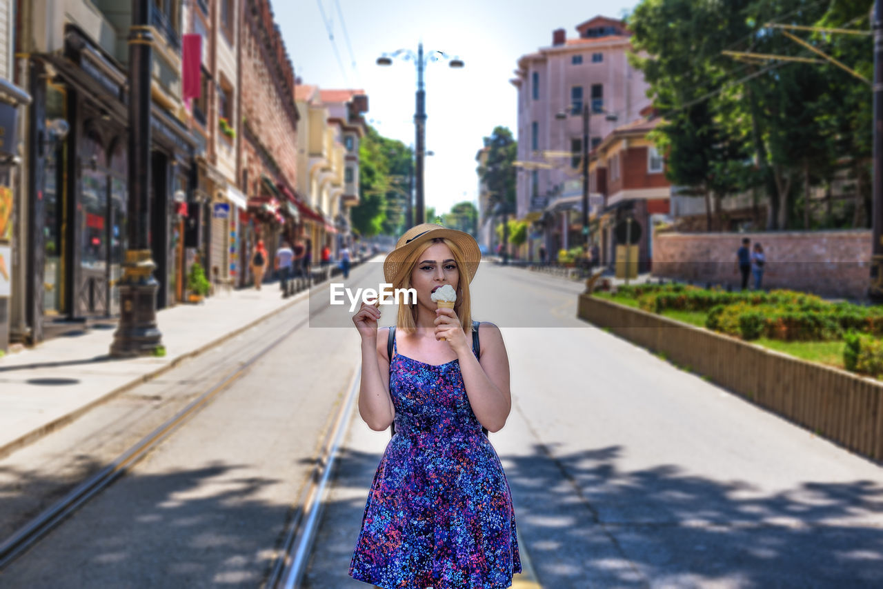 Portrait of smiling young woman eating ice cream on road in city