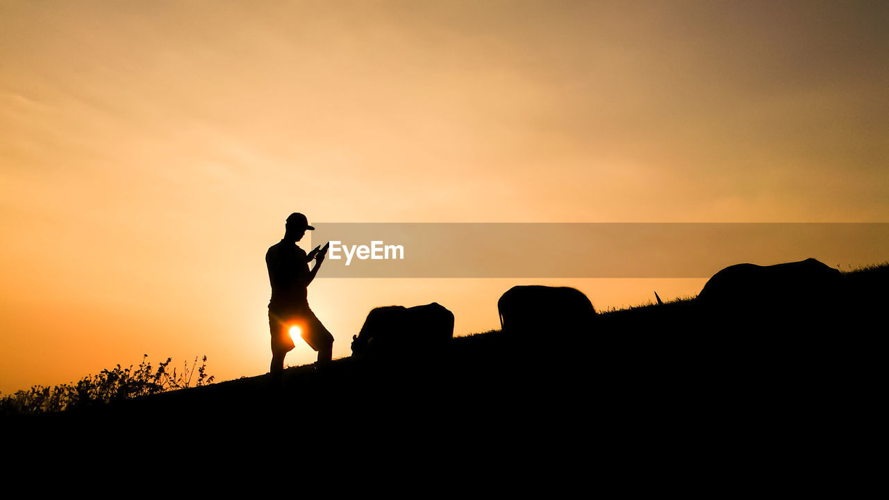 Low angle view of silhouette man using mobile phone on field against orange sky