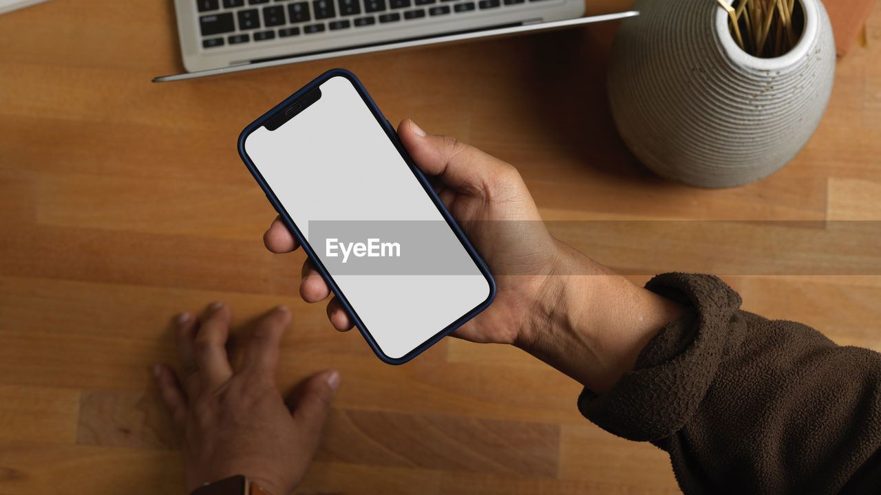 Cropped hand of man holding mobile phone over table