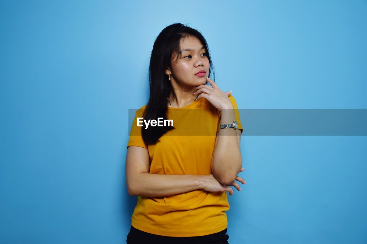 BEAUTIFUL YOUNG WOMAN STANDING AGAINST BLUE BACKGROUND