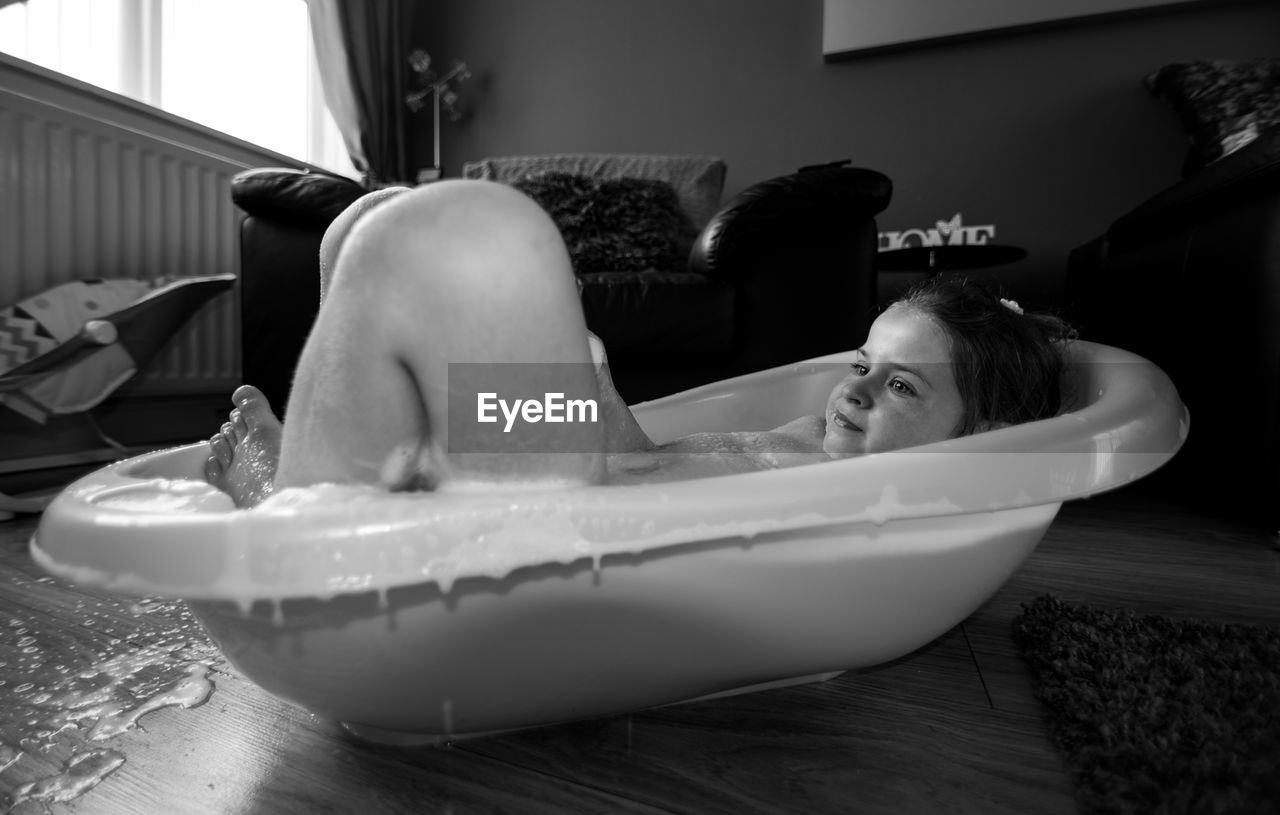 Girl looking away while lying in bath tub at home