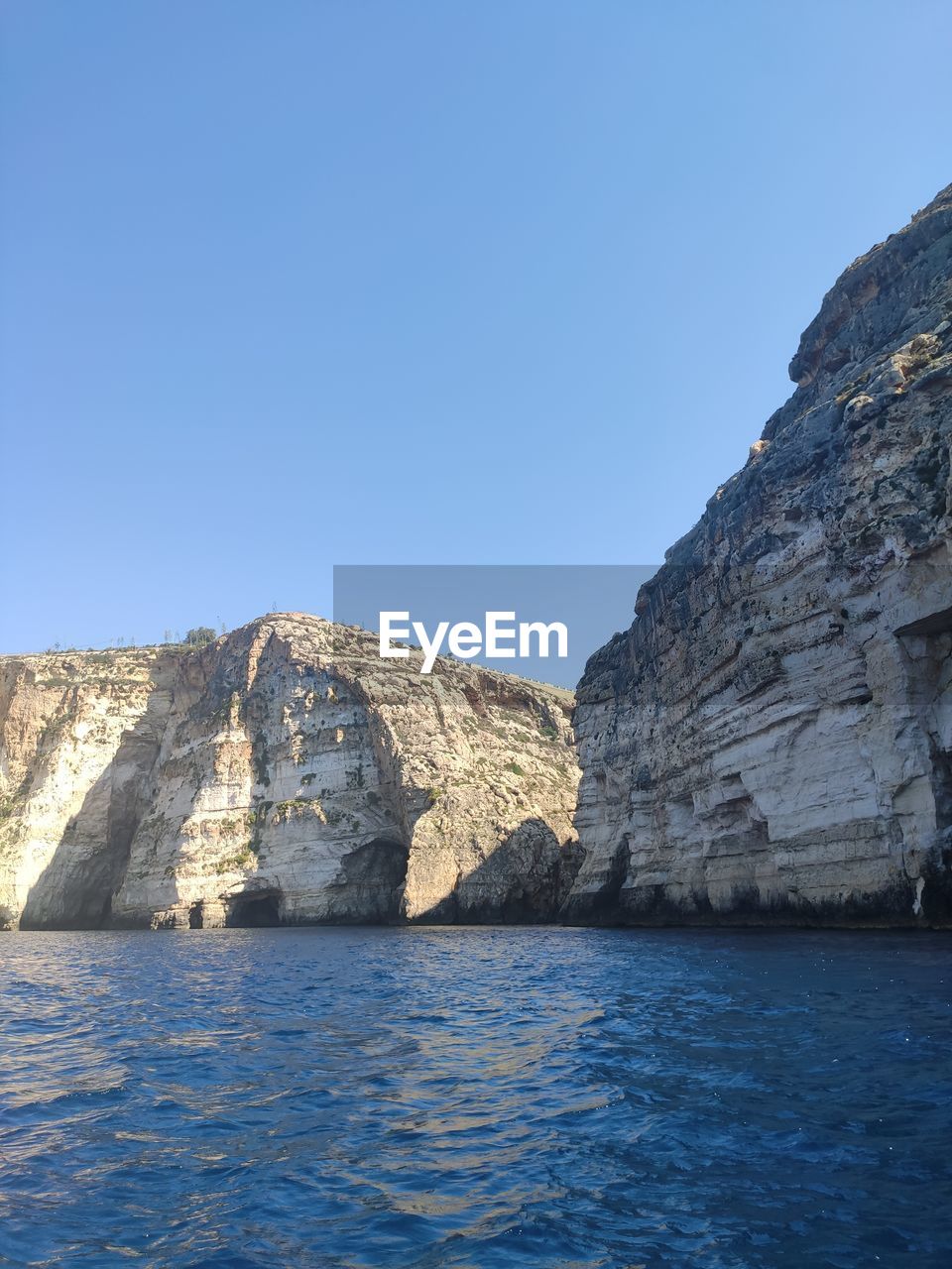 blue, rock, nature, sky, day, architecture, no people, clear sky, outdoors, built structure, low angle view, history, cliff, rock formation, sunlight, terrain, wall, reflection, sunny, the past, sea, travel destinations, wall - building feature, beauty in nature, tranquility