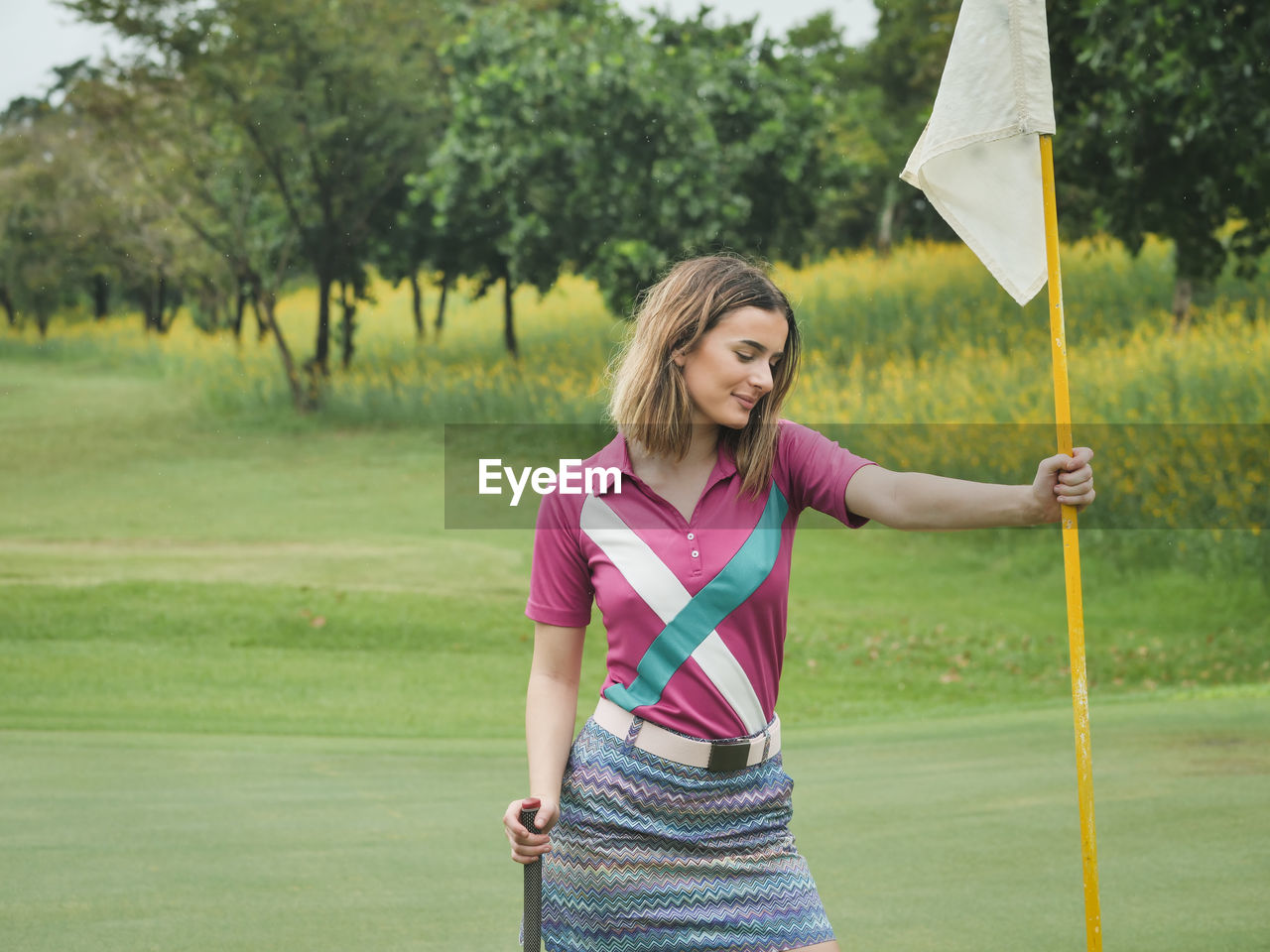 Young woman holding flag while standing on golf course