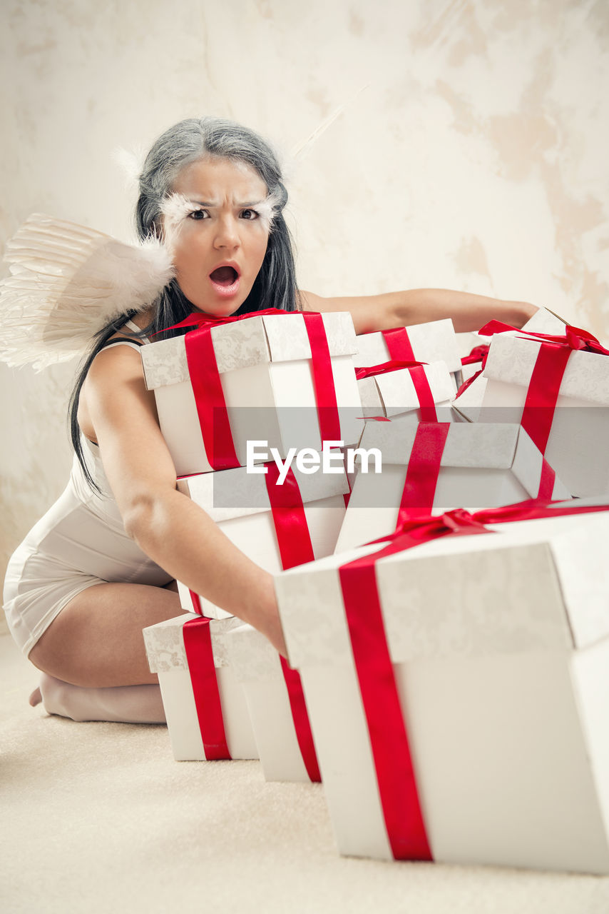 Portrait of angry female model in angel costume holding christmas presents