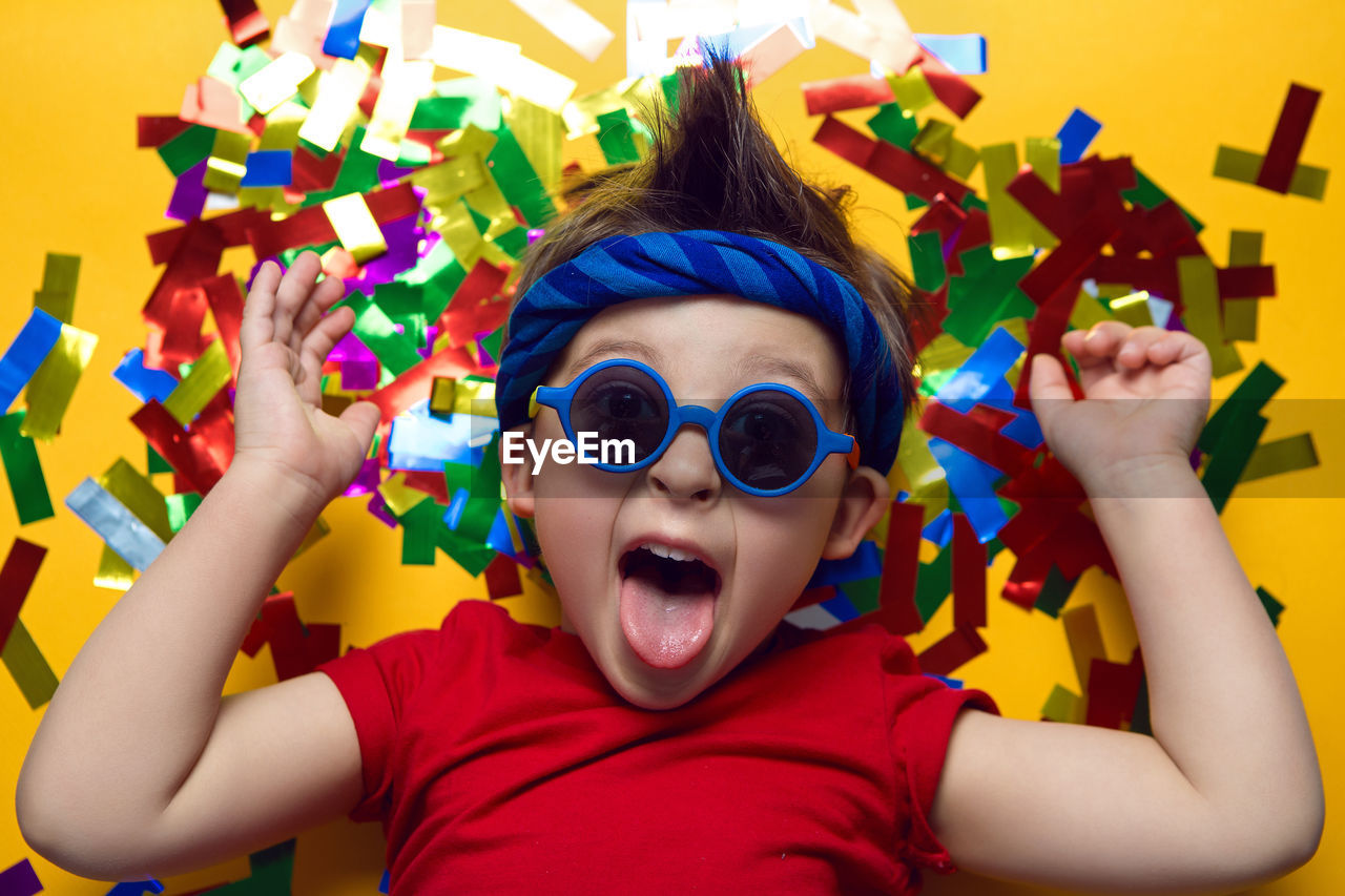 Child a boy in a red t shirt and sunglasses is lying on yellow paper resting at home