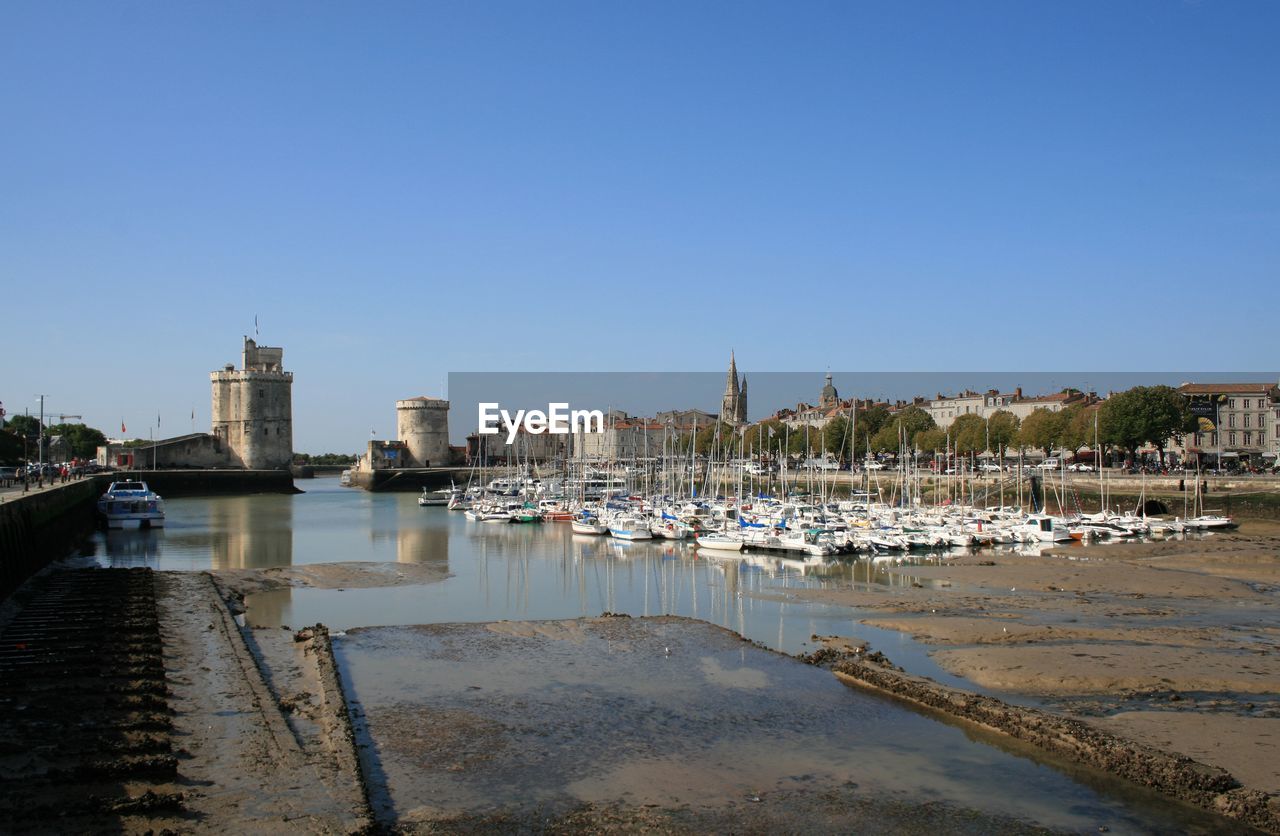 Sailboats moored in harbor by buildings against clear sky