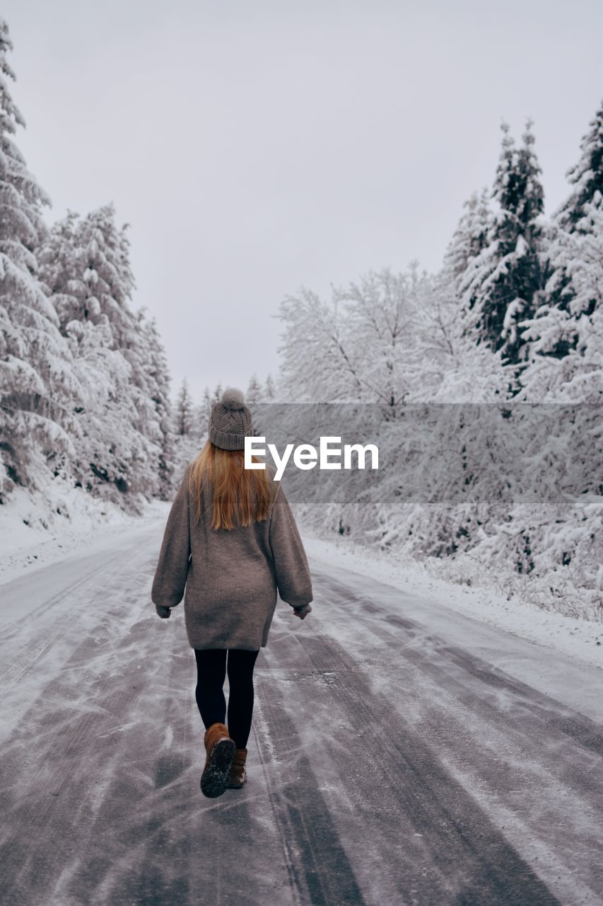 Rear view of woman walking on snow covered road