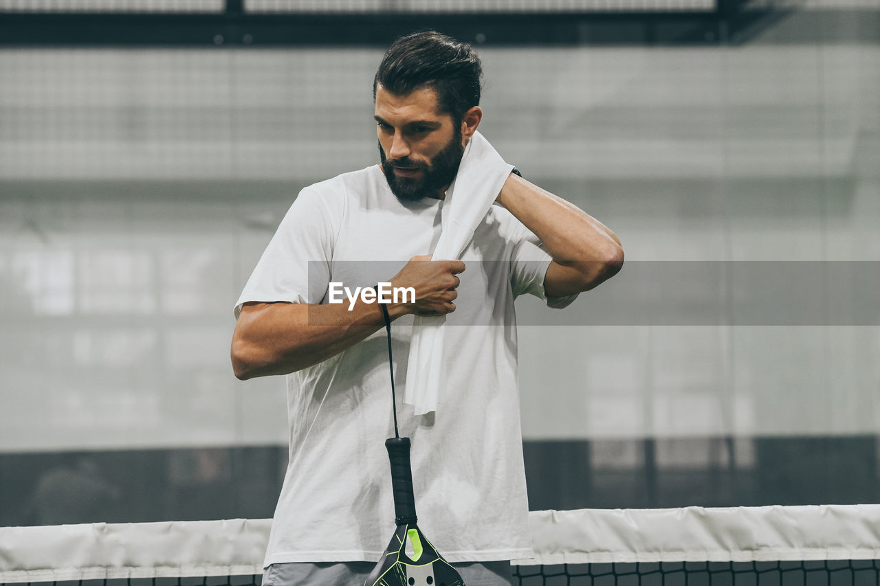 Beautiful man playing padel tennis racket in hand wipes the sweat. young sporty boy after the match