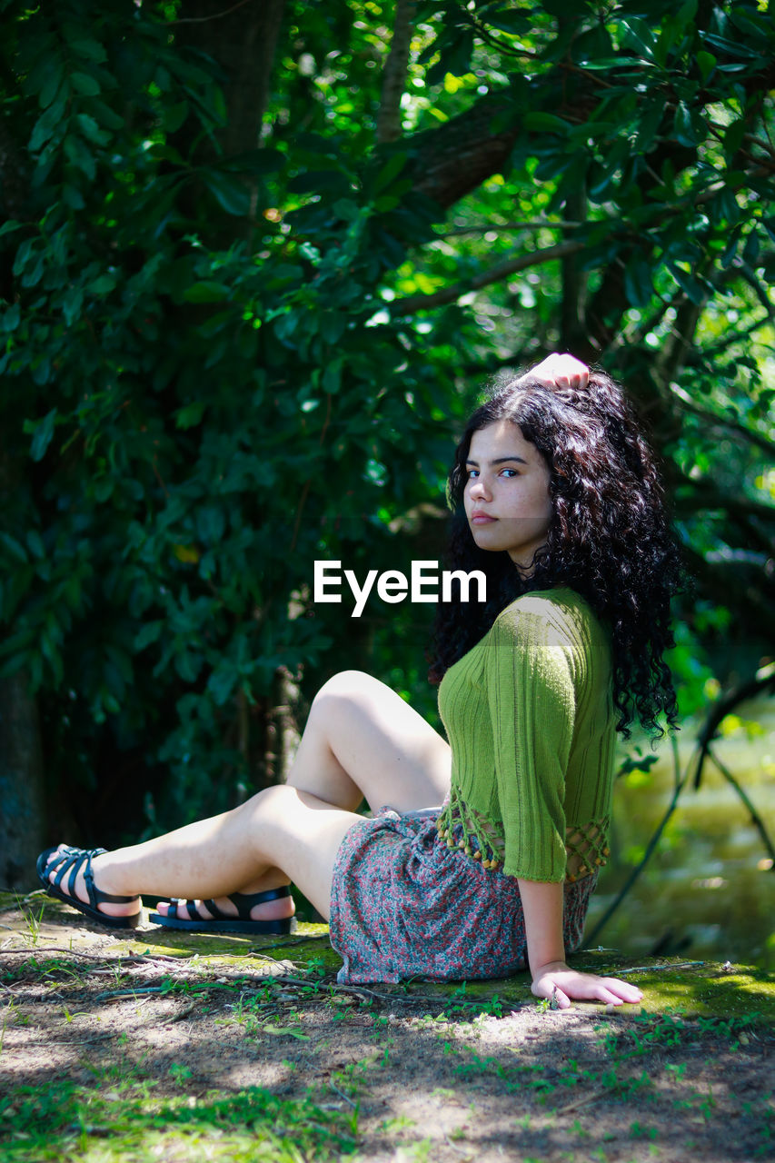 Side view of young woman sitting on tree