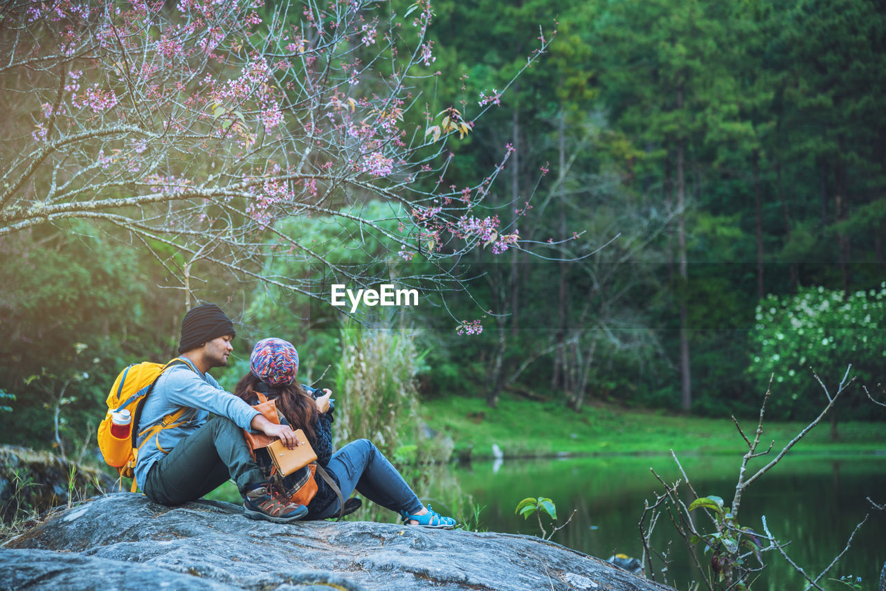 Couple sitting by lake on rock at forest