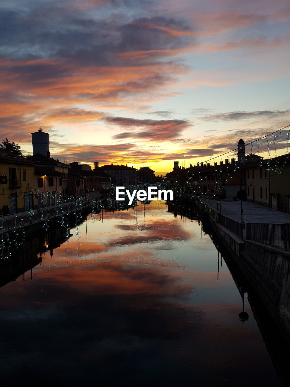 Scenic view of river by buildings against sky during sunset