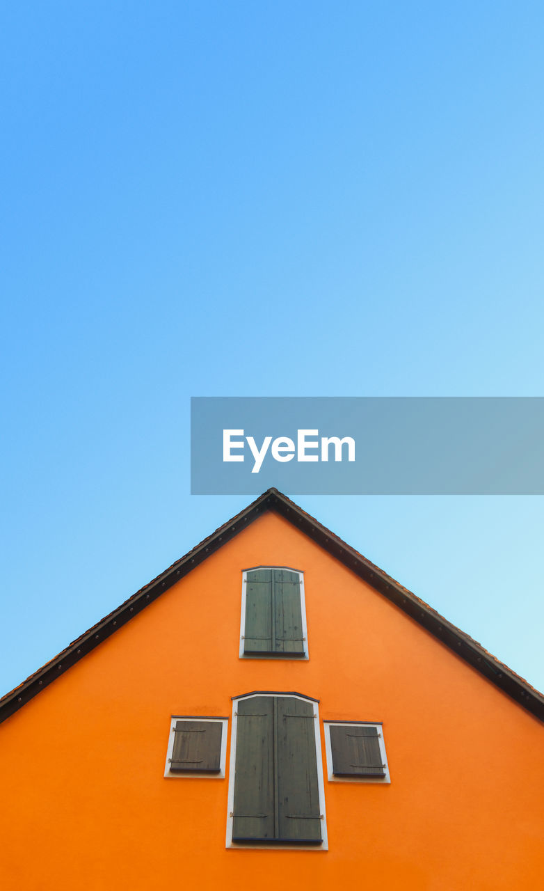 Orange house with pitched roof  on a blue sky. german home with orange walls and timber shutters.