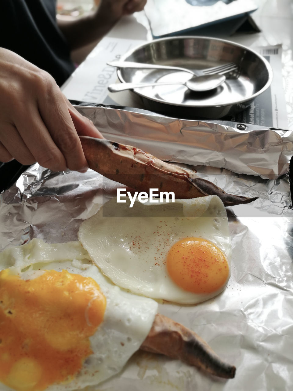 Cropped hand holding roasted sweet potato with fried egg at table