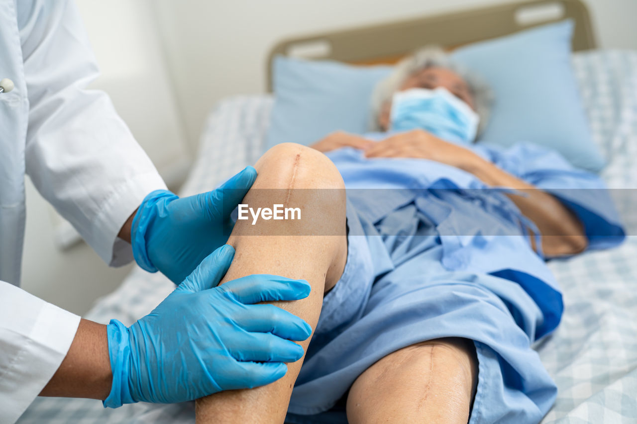 low section of doctor examining patient lying on bed at home